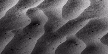 Black and white image highlighting the intricate shadow patterns of sand dunes. Natural abstract art.