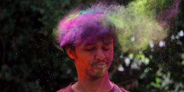 Capture of a man celebrating Holi with vibrant colored powder outdoors.