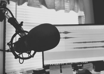 Black and white image of a podcast setup with microphone and waveform screen.