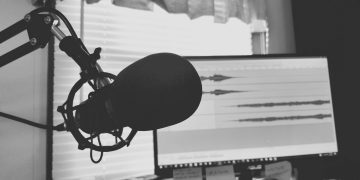 Black and white image of a podcast setup with microphone and waveform screen.