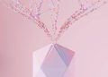 A modern abstract geometric vase with a colorful particle explosion on a pink background.