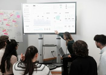 Group of professionals engaged in a business presentation examining charts on a large screen.