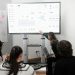 Group of professionals engaged in a business presentation examining charts on a large screen.