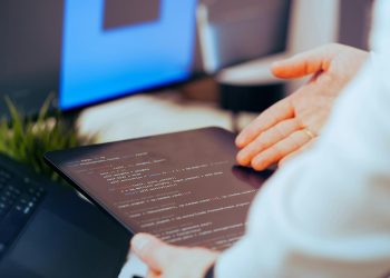 Software developer analyzing code on a tablet in a modern office workspace.
