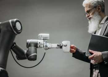 An elderly man receives a cup from a robotic arm in a modern office setting.