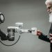 An elderly man receives a cup from a robotic arm in a modern office setting.