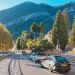 Picturesque town road with parked cars and statues against a mountain backdrop.