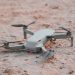 Close-up of a modern drone resting on sandy terrain, highlighting technology and exploration.