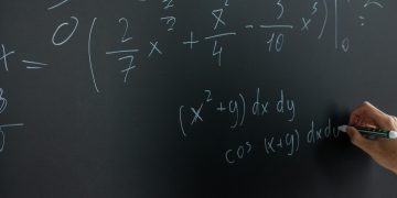 Hand writing mathematical equations on a chalkboard in a classroom setting.