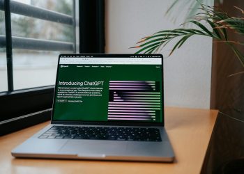 A laptop displaying ChatGPT on a desk by a window, featuring a modern home office setup.