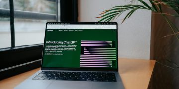 A laptop displaying ChatGPT on a desk by a window, featuring a modern home office setup.