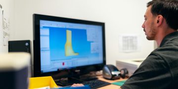 Engineer working on prosthetic design using specialized software in an office setting.
