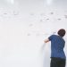 Man in beanie brainstorming and writing flowchart on office whiteboard, planning ideas.