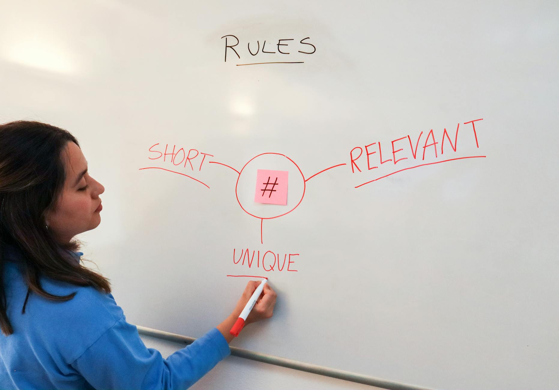 Woman illustrating marketing rules with hashtags on a whiteboard for effective branding strategies.
