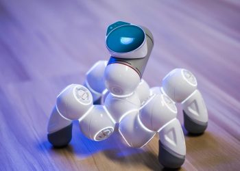A sleek, white robotic toy on a wooden floor with a blurred background and blue lighting.
