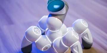 A sleek, white robotic toy on a wooden floor with a blurred background and blue lighting.