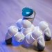 A sleek, white robotic toy on a wooden floor with a blurred background and blue lighting.