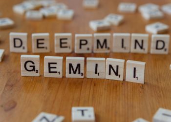 Wooden Scrabble tiles spelling 'Deepmind' and 'Gemini' on a wooden surface, a concept of AI and games.