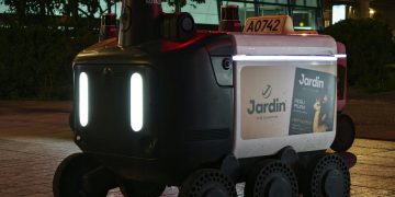 Close-up view of an autonomous delivery robot on a city street at night under artificial light.