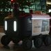 Close-up view of an autonomous delivery robot on a city street at night under artificial light.