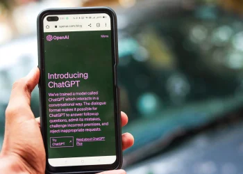 Close-up of a smartphone showing ChatGPT details on the OpenAI website, held by a person.