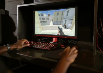 Person engaging in a shooting video game on a high-performance setup with mechanical keyboard.