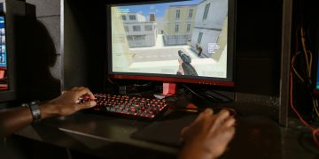 Person engaging in a shooting video game on a high-performance setup with mechanical keyboard.