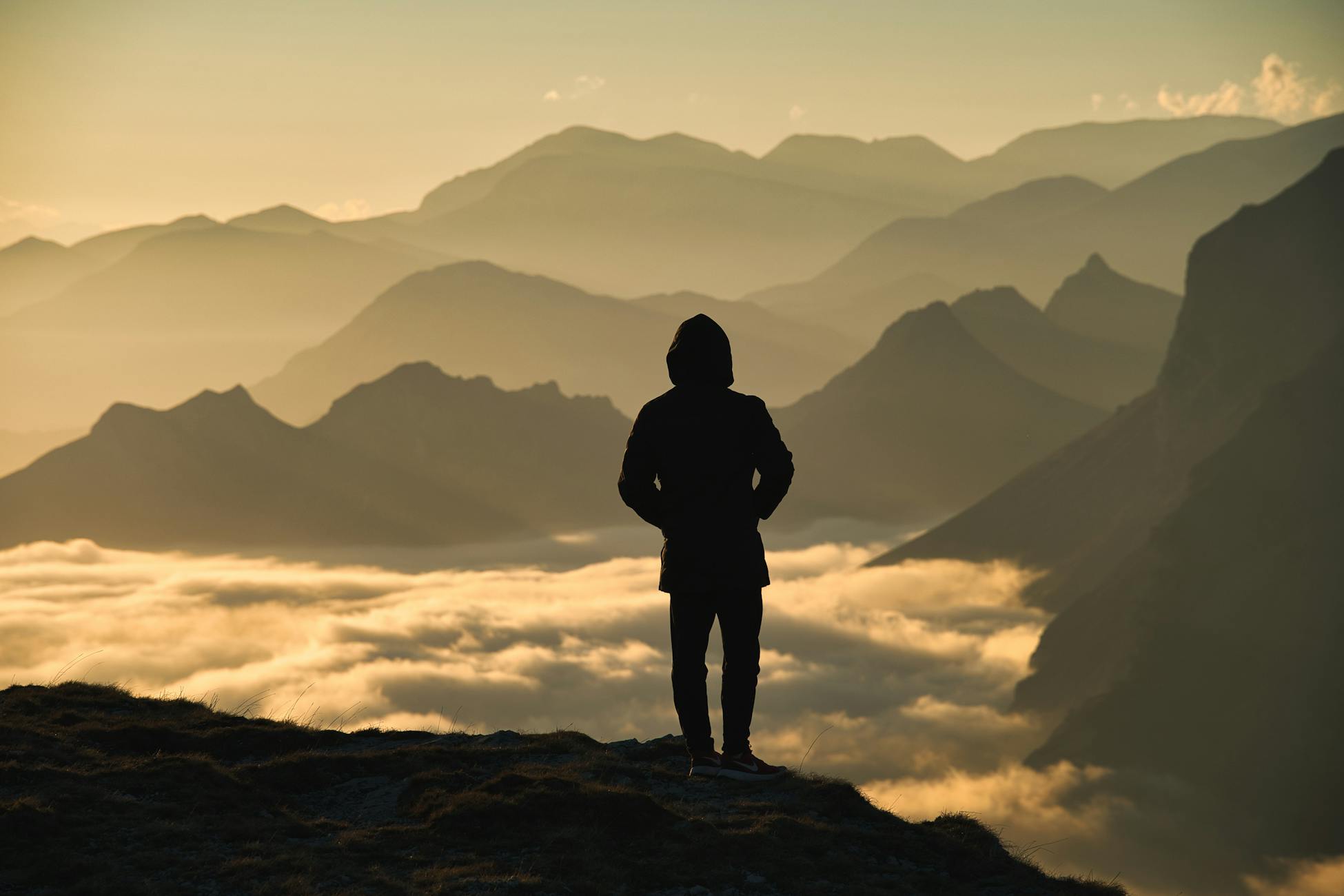 Silhouette of person overlooking misty mountains with dramatic sunrise lighting.