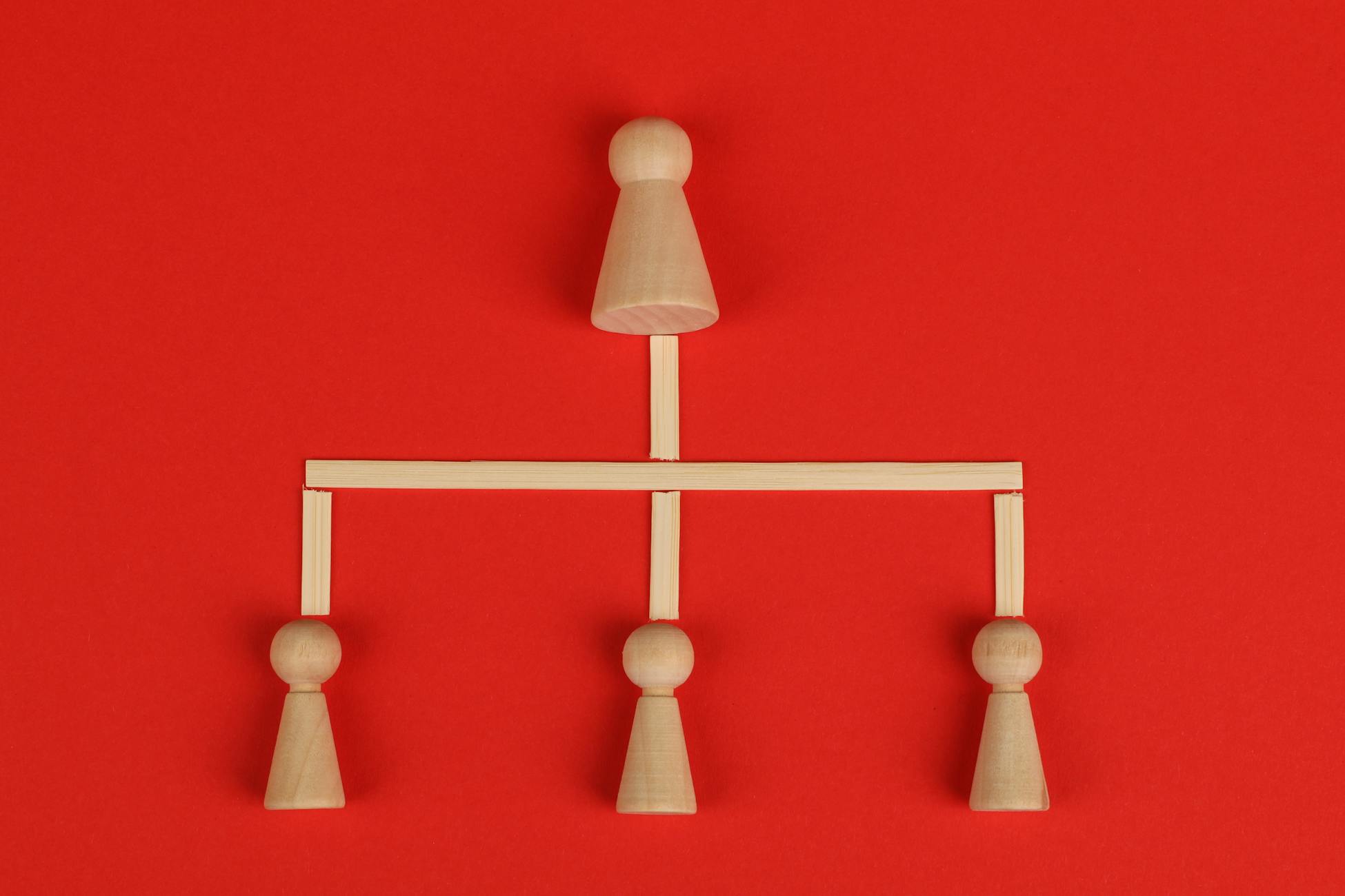 Conceptual depiction of hierarchy using wooden pieces on a vibrant red background.