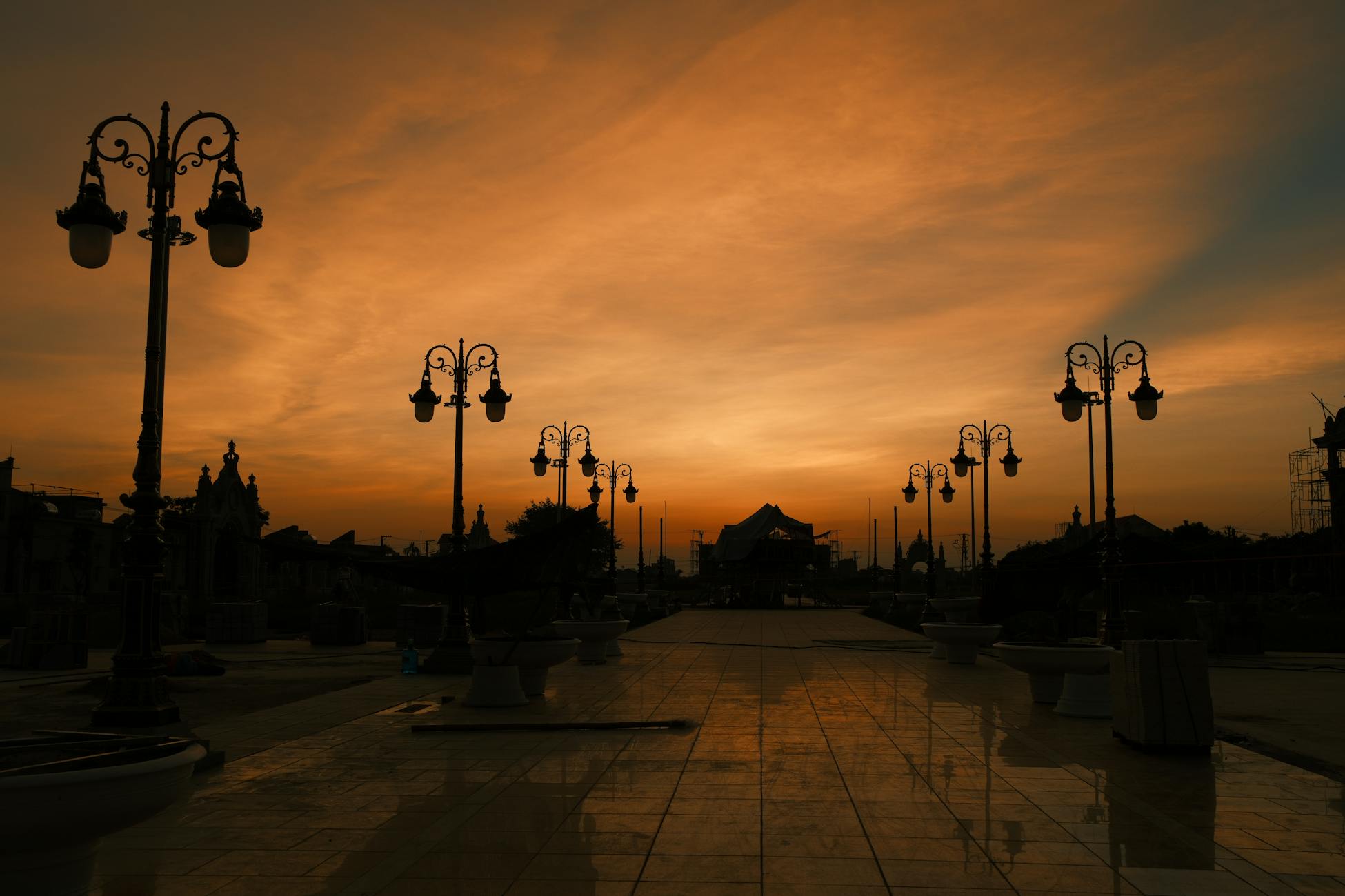 Dramatic sunset sky with silhouette of vintage street lamps and architecture reflecting on tiles.