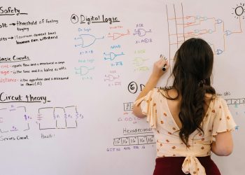 Female student writing circuit diagrams and logic gates in an educational setting on a whiteboard.