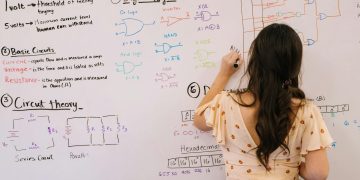 Female student writing circuit diagrams and logic gates in an educational setting on a whiteboard.