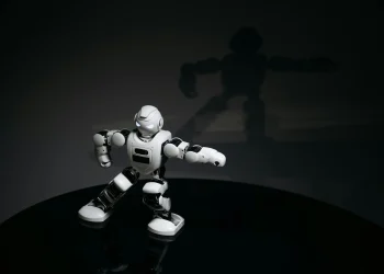 A futuristic white toy robot striking a pose in a dimly lit studio with a shadow cast behind it.