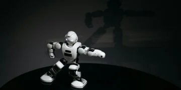 A futuristic white toy robot striking a pose in a dimly lit studio with a shadow cast behind it.