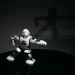 A futuristic white toy robot striking a pose in a dimly lit studio with a shadow cast behind it.