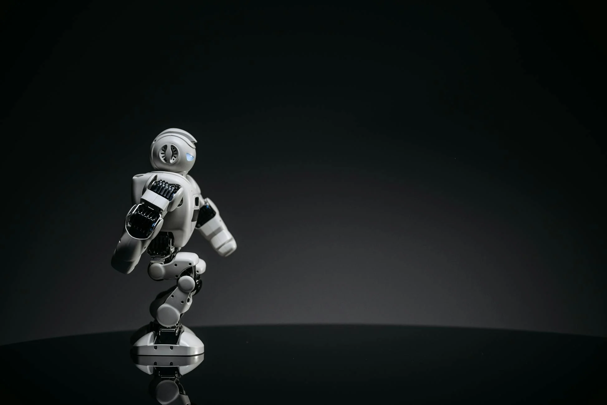 A sleek white toy robot poised elegantly against a dark studio backdrop.