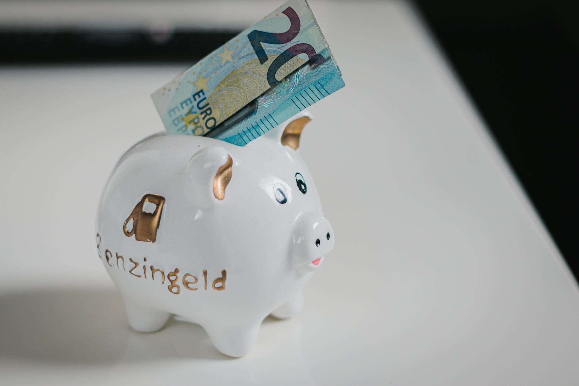 A white piggy bank with a €20 note inserted, symbolizing savings.
