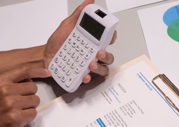 Close-up of hands using a calculator next to a company invoice, depicting a financial calculation concept.