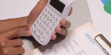Close-up of hands using a calculator next to a company invoice, depicting a financial calculation concept.
