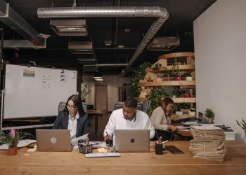 Three professionals focused on work in a stylish office with laptops and documents.