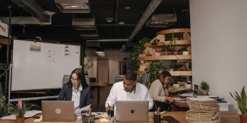 Three professionals focused on work in a stylish office with laptops and documents.