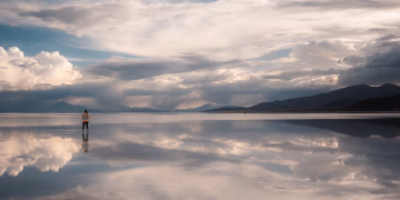 Serene scene of a traveler at Uyuni Salt Flats with stunning reflections and sky.
