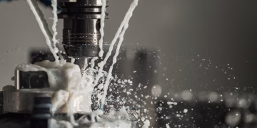 Dynamic close-up of CNC machine with coolant splashing during metalwork operation.