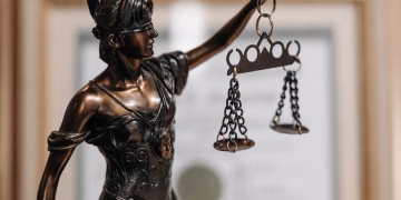 Close-up of a bronze Lady Justice statue holding scales in an office environment.