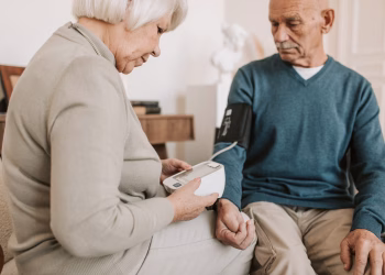 Senior couple at home using a sphygmomanometer to monitor blood pressure, promoting elderly health care.