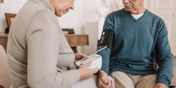 Senior couple at home using a sphygmomanometer to monitor blood pressure, promoting elderly health care.