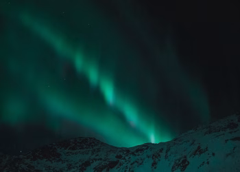 Majestic aurora borealis illuminates the night sky over snow-covered mountains.