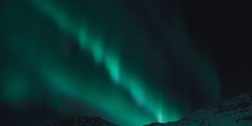 Majestic aurora borealis illuminates the night sky over snow-covered mountains.
