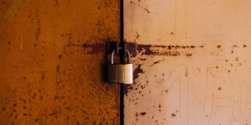 A close-up view of a rusty padlock securing a weathered metal door, highlighting decay and security.