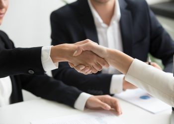 two people shaking hands in front of a laptop